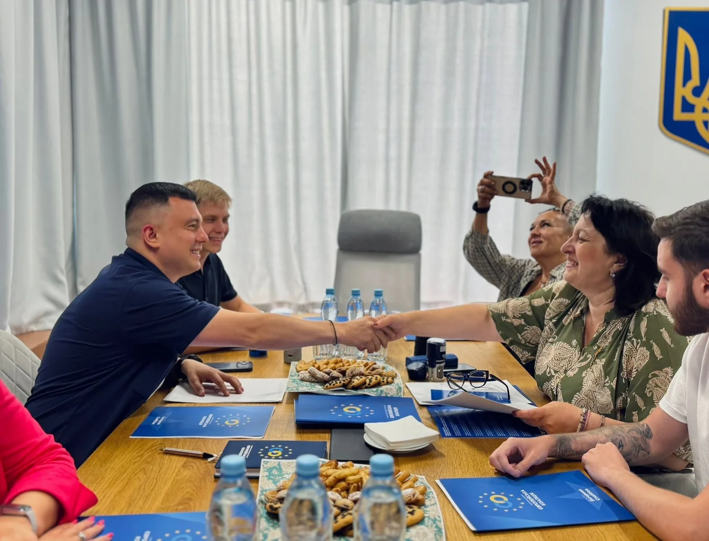 A handshake during a meeting at the negotiating table, with folders bearing the «Європейська Коаліція» emblem on the table