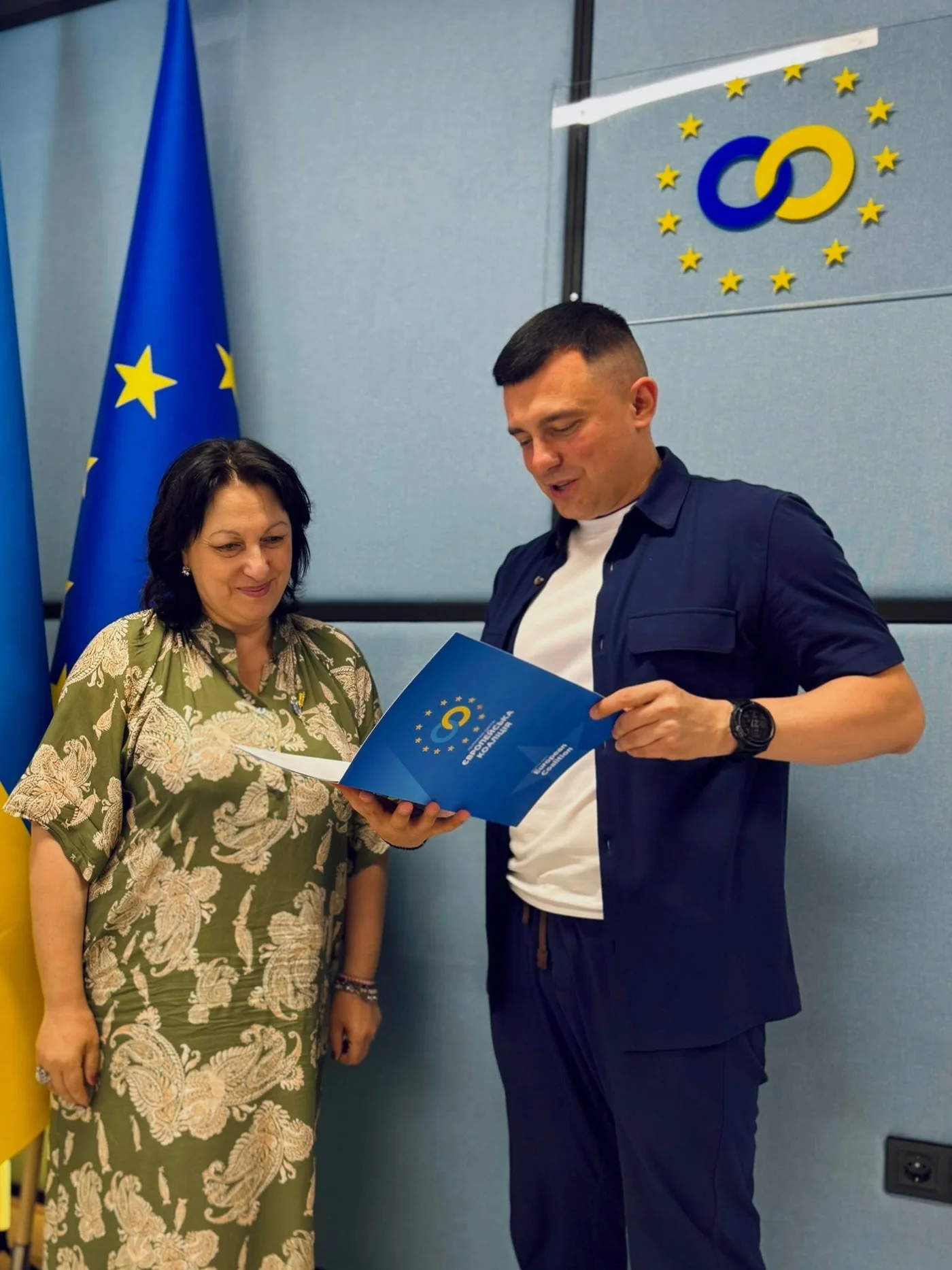 Handing over a folder bearing the «Європейська Коаліція» emblem in front of the EU flag